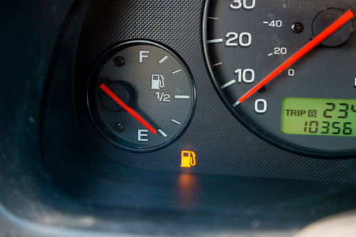 A gas guage in a car reads empty and shows the warning light to let the driver know they are out of gas and need to refuel.